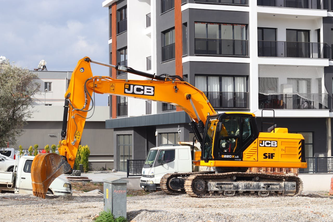 A yellow excavator operating at a city construction site in front of modern buildings.